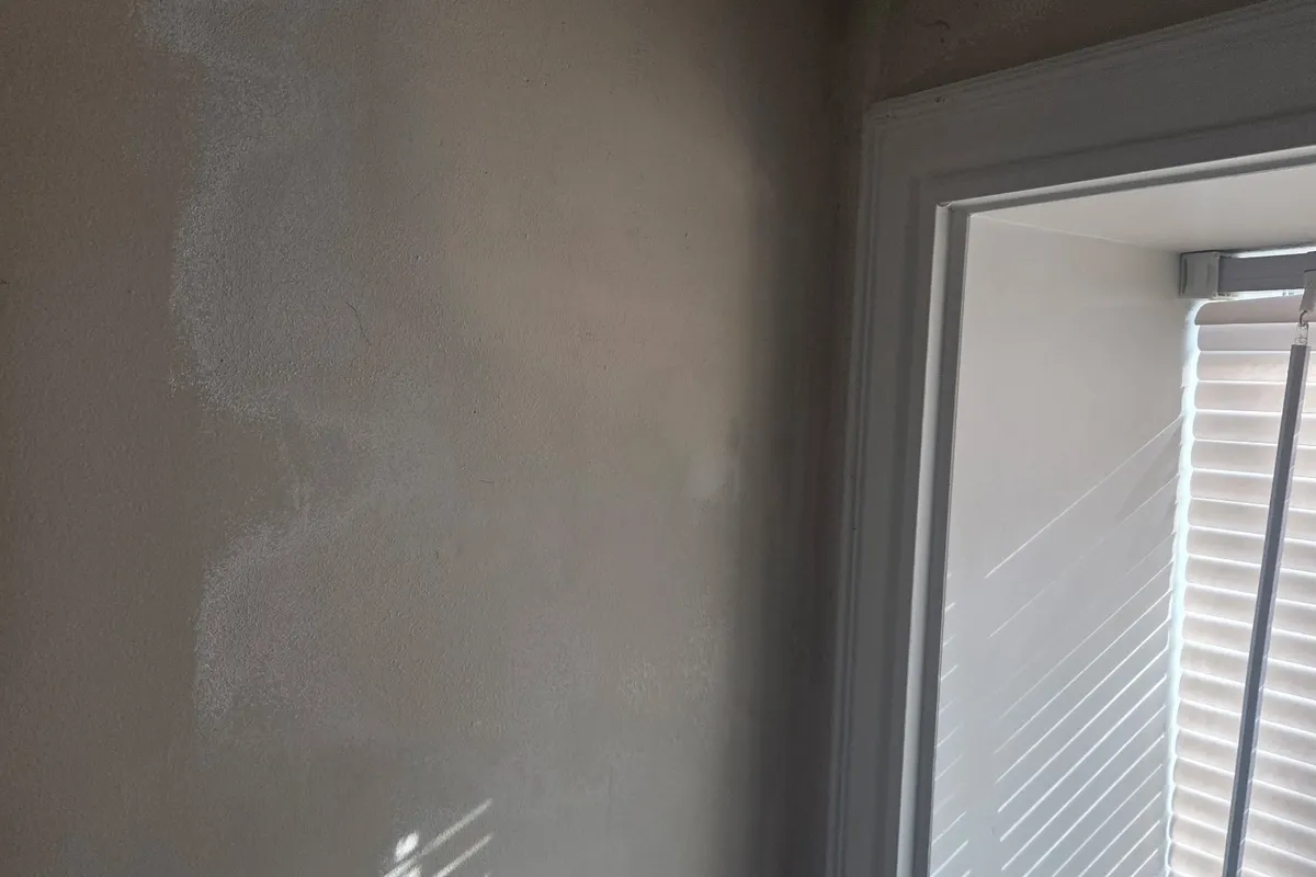 Smooth, painted drywall wall beside a white-trimmed window with a texture-matched repair blended into the surface