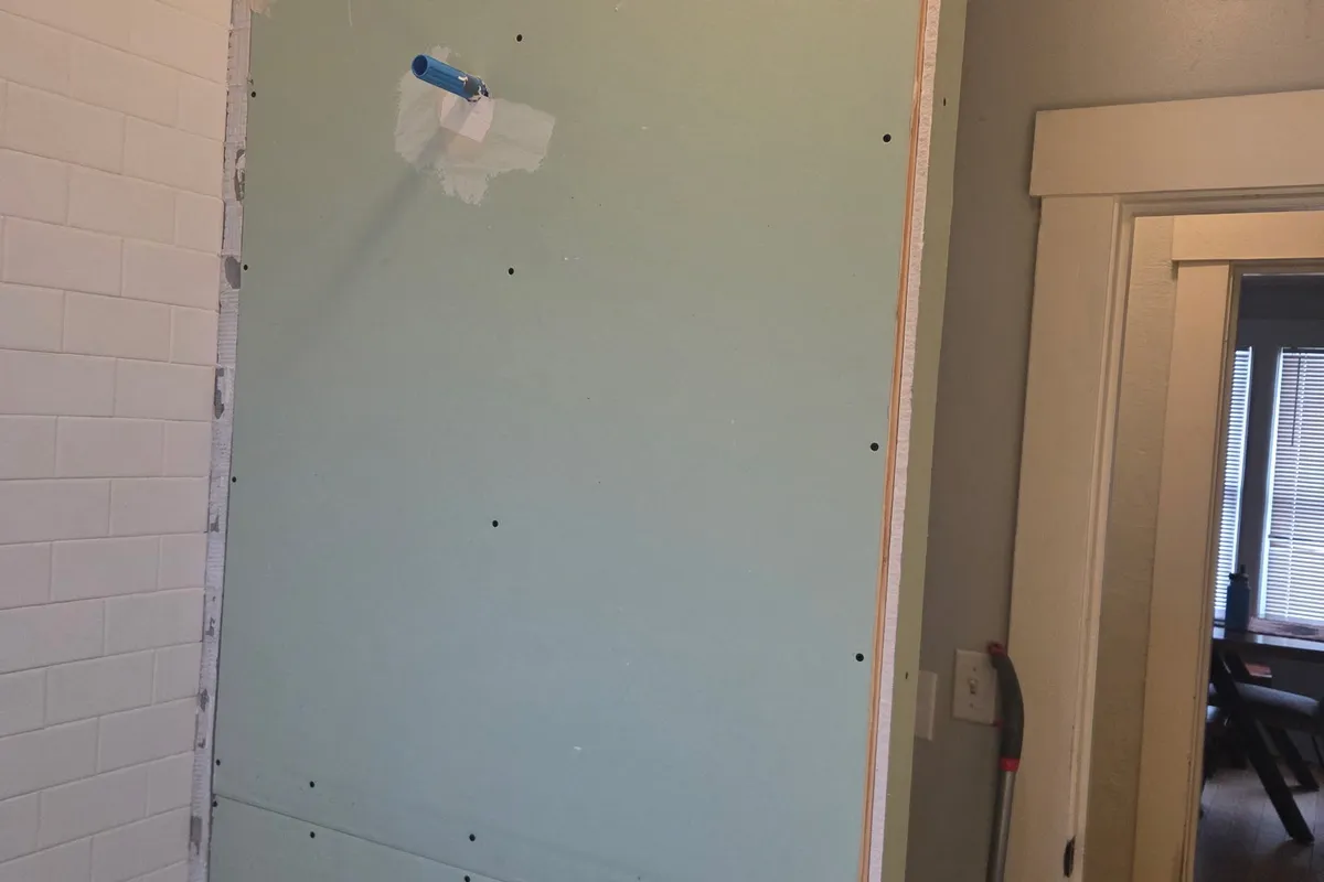 Newly installed moisture-resistant drywall next to subway tile with a plumbing stub-out, mid-installation