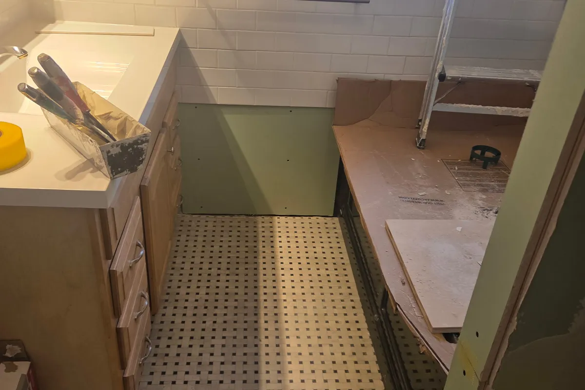 Bathroom remodel in progress with a fresh drywall patch below the vanity and taping knives on the counter