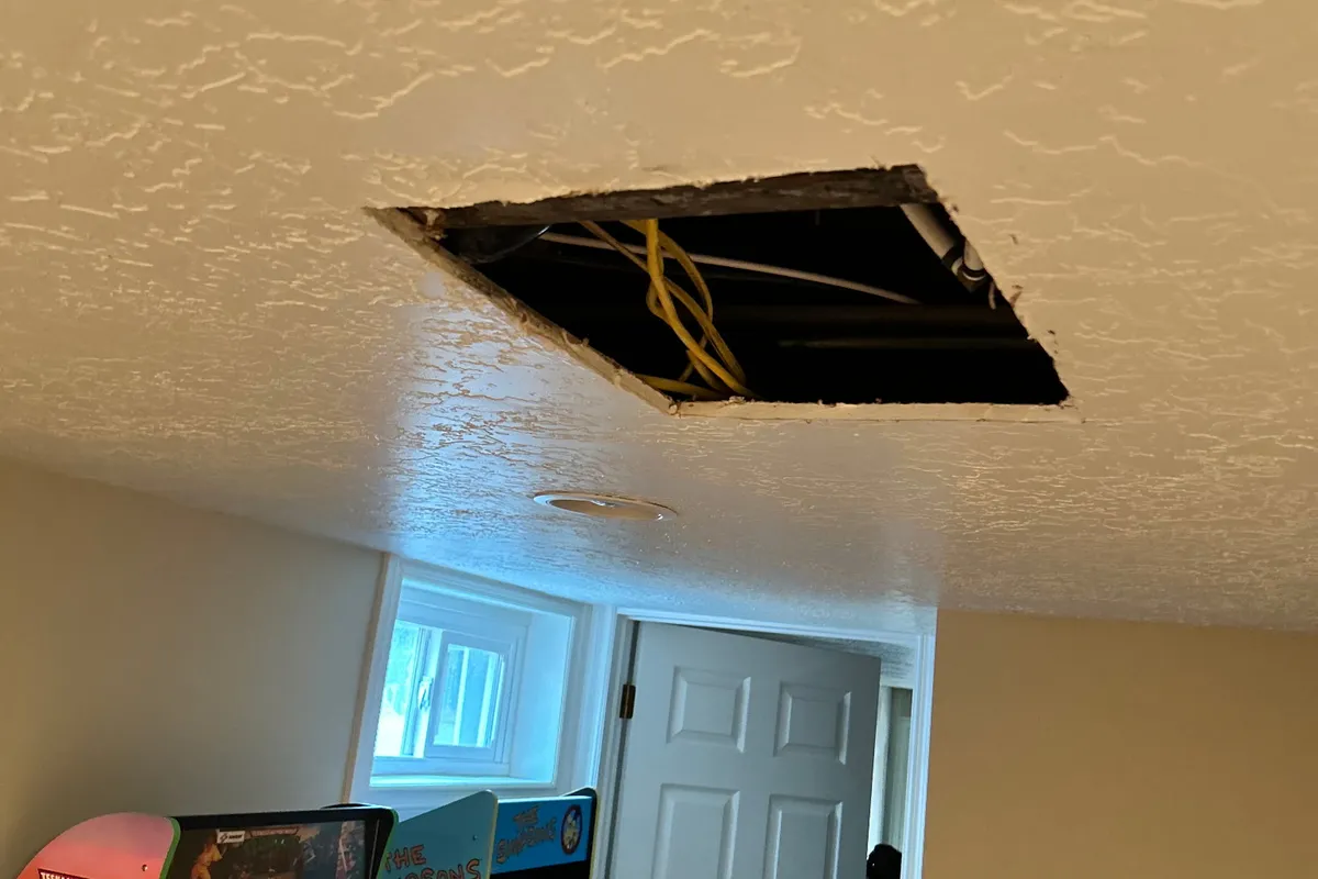 Textured ceiling with a clean square access cut exposing wiring, prepped for patching